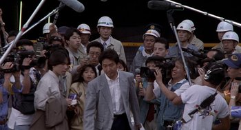 Movie still from “Godzilla vs. Destoroyah” (1995), directed by Ishirô Honda – A group of people gathered around a man in a gray suit; Medium shot, Over the shoulder angle