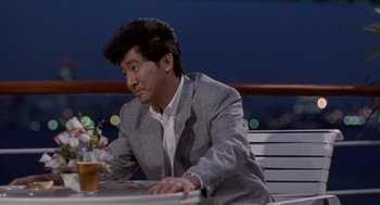 Movie still from “Godzilla vs. Destoroyah” (1995), directed by Ishirô Honda – A man sitting at a table with a drink in front of him; Medium shot, Over the shoulder angle
