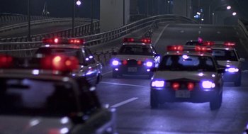 Movie still from “Godzilla vs. Destoroyah” (1995), directed by Ishirô Honda – A group of police cars driving down a street at night; Wide shot, High angle