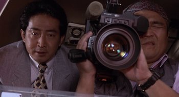 Movie still from “Godzilla vs. Destoroyah” (1995), directed by Ishirô Honda – A man in a suit is holding a video camera; Close Up shot, Low angle