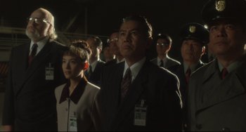 Movie still from “Godzilla vs. Mechagodzilla II” (1993), directed by Kazuki Ômori – A group of men and women standing in a dark room; Medium shot, Low angle