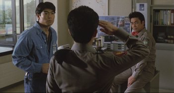 Movie still from “Godzilla vs. Mechagodzilla II” (1993), directed by Kazuki Ômori – A man saluting in front of a group of people; Medium shot, Over the shoulder angle