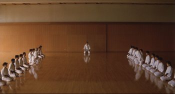 Movie still from “Godzilla vs. Mechagodzilla II” (1993), directed by Kazuki Ômori – A group of people sitting on the floor of an empty room; Extreme Wide shot, High angle