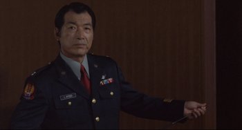 Movie still from “Godzilla vs. Mechagodzilla II” (1993), directed by Kazuki Ômori – A man in a military uniform is holding something in his hand; Medium shot, Low angle