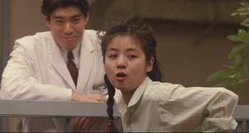 Movie still from “Godzilla vs. Mechagodzilla II” (1993), directed by Kazuki Ômori – A young woman with a pigtail standing next to a man; Medium shot, Low angle