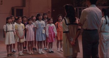 Movie still from “Godzilla vs. Mechagodzilla II” (1993), directed by Kazuki Ômori – A group of young girls standing next to each other in front of an older woman; Medium shot, High angle