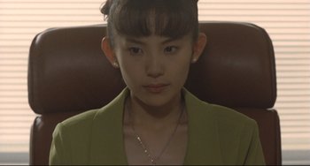 Movie still from “Godzilla vs. Mechagodzilla II” (1993), directed by Kazuki Ômori – A young woman sitting in a chair wearing a green jacket; Close Up shot, High angle
