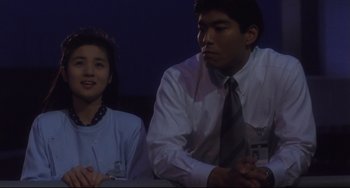 Movie still from “Godzilla vs. Mechagodzilla II” (1993), directed by Kazuki Ômori – A man and a woman sitting next to each other at a table; Medium shot, Low angle