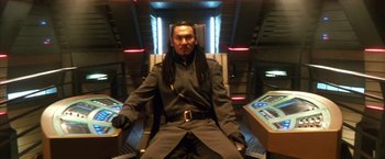 Movie still from “Godzilla: Final Wars” (2004), directed by Koji Hashimoto – A man sitting in a chair in front of a computer screen; Medium shot, High angle