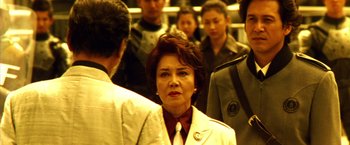 Movie still from “Godzilla: Final Wars” (2004), directed by Koji Hashimoto – An older woman in a white jacket and a tie; Close Up shot, Over the shoulder angle