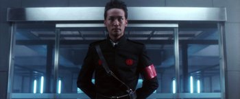 Movie still from “Godzilla: Final Wars” (2004), directed by Koji Hashimoto – A man in a uniform is standing in front of a building; Close Up shot, Low angle