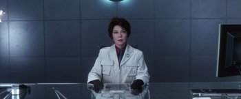 Movie still from “Godzilla: Final Wars” (2004), directed by Koji Hashimoto – A woman sitting at a table wearing a lab coat; Medium shot, Low angle