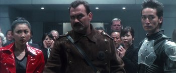 Movie still from “Godzilla: Final Wars” (2004), directed by Koji Hashimoto – A man in a brown jacket is standing in front of a group of people; Close Up shot, Low angle