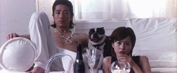 Movie still from “Godzilla: Final Wars” (2004), directed by Koji Hashimoto – A man and a woman sitting at a table with a dog; Medium shot, Low angle