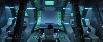 Movie still from “Godzilla: Final Wars” (2004), directed by Koji Hashimoto – A person sitting in a chair in front of a computer screen; Wide shot, Overhead angle