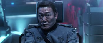 Movie still from “Godzilla: Final Wars” (2004), directed by Koji Hashimoto – A person sitting in a chair wearing a uniform; Close Up shot, Low angle
