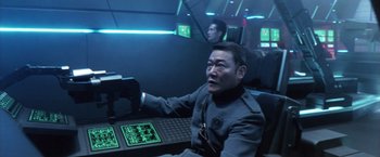 Movie still from “Godzilla: Final Wars” (2004), directed by Koji Hashimoto – A man sitting at a table in a room; Medium shot, High angle