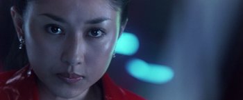 Movie still from “Godzilla: Final Wars” (2004), directed by Koji Hashimoto – A woman's face in front of blurry lights; Close Up shot, Low angle