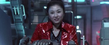 Movie still from “Godzilla: Final Wars” (2004), directed by Koji Hashimoto – A woman in a red jacket sitting in an office chair; Close Up shot, Low angle
