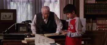 Movie still from “Godzilla: Tokyo S.O.S.” (2003), directed by Takao Okawara – An older man and a young boy looking at a book; Medium shot, Low angle