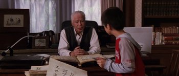 Movie still from “Godzilla: Tokyo S.O.S.” (2003), directed by Takao Okawara – An older man sitting at a desk with a young boy; Medium shot, Over the shoulder angle