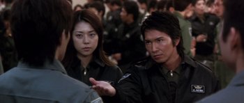 Movie still from “Godzilla: Tokyo S.O.S.” (2003), directed by Takao Okawara – A man and a woman are standing in front of a group of people; Close Up shot, Over the shoulder angle