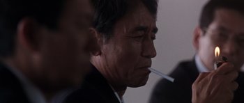 Movie still from “Godzilla: Tokyo S.O.S.” (2003), directed by Takao Okawara – An older man is smoking a cigarette in a dark room; Close Up shot, Low angle