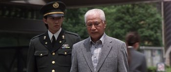 Movie still from “Godzilla: Tokyo S.O.S.” (2003), directed by Takao Okawara – An older man in a suit and a military uniform stands in front of an older man in a suit; Medium shot, Low angle