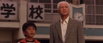 Movie still from “Godzilla: Tokyo S.O.S.” (2003), directed by Takao Okawara – A man and a boy standing next to each other in front of a building; Medium shot, Low angle