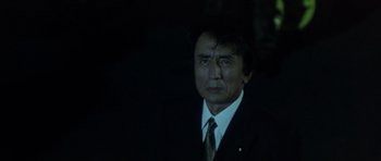Movie still from “Godzilla: Tokyo S.O.S.” (2003), directed by Takao Okawara – A man wearing a suit and tie standing in the dark; Close Up shot, Low angle