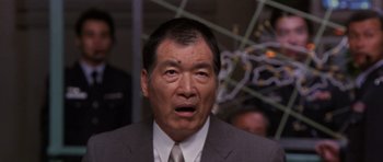 Movie still from “Godzilla: Tokyo S.O.S.” (2003), directed by Takao Okawara – An older man in a gray suit and white tie; Close Up shot, Low angle