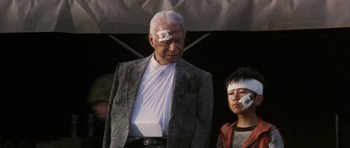 Movie still from “Godzilla: Tokyo S.O.S.” (2003), directed by Takao Okawara – An older man with bandages on his head and a young boy with bandages on his face; Medium shot, Low angle