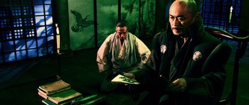 Movie still from “Goemon” (2009), directed by Kazuaki Kiriya – Two men sitting on the ground in front of a painting; Medium shot, Low angle