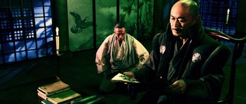 Movie still from “Goemon” (2009), directed by Kazuaki Kiriya – Two men sitting on the ground in front of a painting; Medium shot, Low angle