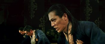 Movie still from “Goemon” (2009), directed by Kazuaki Kiriya – A man with long black hair is wearing a black and gold shirt; Close Up shot, Low angle