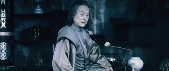 Movie still from “Goemon” (2009), directed by Kazuaki Kiriya – An older woman sitting in front of a pot of food; Medium shot, Low angle