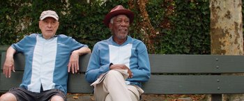 Movie still from “Going in Style” (2017), directed by Zach Braff – An older man sitting on top of a wooden bench; Medium shot, Over the shoulder angle