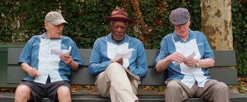 Movie still from “Going in Style” (2017), directed by Zach Braff – A group of people sitting on top of a wooden bench; Medium shot, Low angle