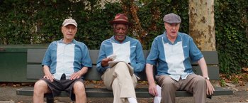 Movie still from “Going in Style” (2017), directed by Zach Braff – A group of men sitting on top of a wooden bench; Medium shot, Low angle
