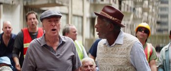 Movie still from “Going in Style” (2017), directed by Zach Braff – Two older men talking to each other in a crowd; Medium shot, Over the shoulder angle