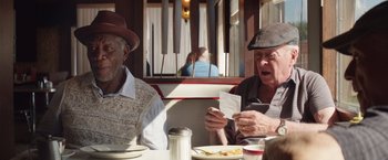 Movie still from “Going in Style” (2017), directed by Zach Braff – Two older men sitting at a table with food in front of them; Medium shot, Over the shoulder angle