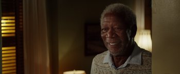 Movie still from “Going in Style” (2017), directed by Zach Braff – An older man smiling for the camera in a living room; Close Up shot, Over the shoulder angle