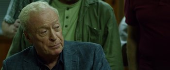 Movie still from “Going in Style” (2017), directed by Zach Braff – An older man sitting in front of a group of people; Close Up shot, Over the shoulder angle