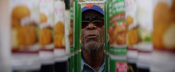 Movie still from “Going in Style” (2017), directed by Zach Braff – An older man wearing sunglasses and a hat is surrounded by cans of food; Close Up shot, Low angle