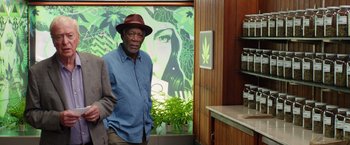 Movie still from “Going in Style” (2017), directed by Zach Braff – A man standing in front of a wall with a painting of a woman; Medium shot, Over the shoulder angle