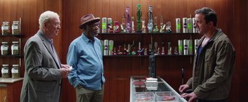 Movie still from “Going in Style” (2017), directed by Zach Braff – An older man standing in front of a shelf of glass; Medium shot, Over the shoulder angle