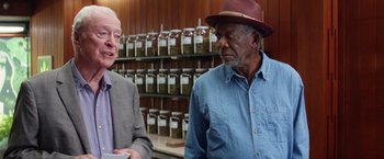 Movie still from “Going in Style” (2017), directed by Zach Braff – Two men are standing next to each other in front of a shelf of herbs; Medium shot, Over the shoulder angle