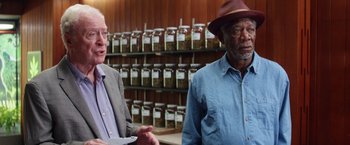Movie still from “Going in Style” (2017), directed by Zach Braff – Two men standing next to each other in front of a room filled with jars; Medium shot, Over the shoulder angle
