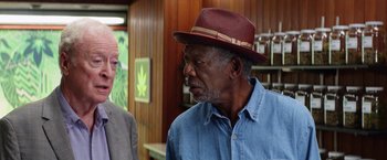 Movie still from “Going in Style” (2017), directed by Zach Braff – A man in a red hat is talking to another man in a blue shirt; Medium shot, Over the shoulder angle