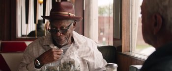 Movie still from “Going in Style” (2017), directed by Zach Braff – An older man sitting in a chair holding a bowl of marijuana; Close Up shot, Over the shoulder angle